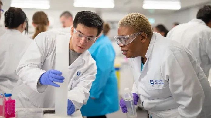Two students with white lab coats on conducting an experiment in a lab at Dundee