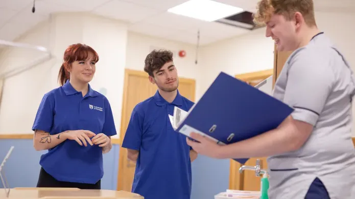 Nurse standing with a clipboard talking to Dundee nursing students at the Clinical Skills Centre