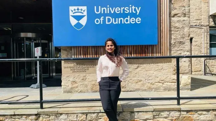 Thusharika standing in front of a large blue University of Dundee sign