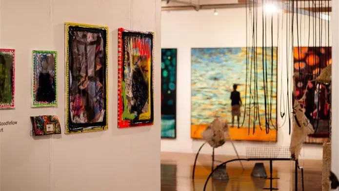 View of two walls with large artworks on them, and sculptures in the middle of a wooden floor