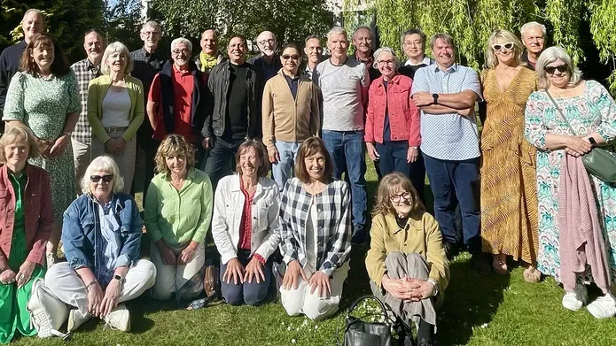 group of people standing in front of tall building on bright sunny day with green trees and grass in foreground