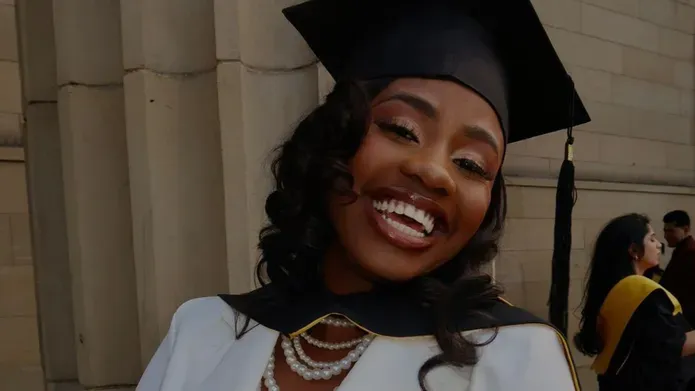 : A close image of a student wearing a white top, with beaded necklace and graduation cap on her head