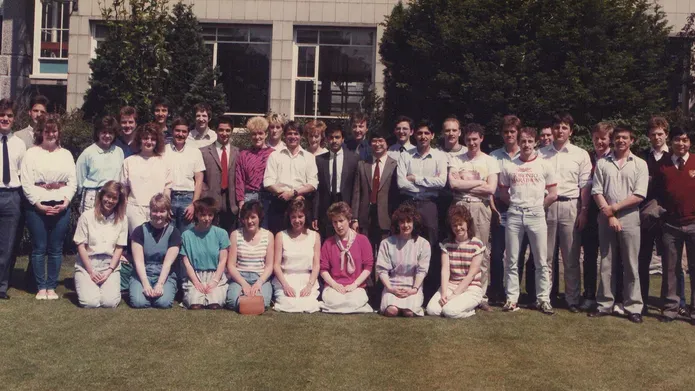 group of students in 1980s clothes on a grassy lawn