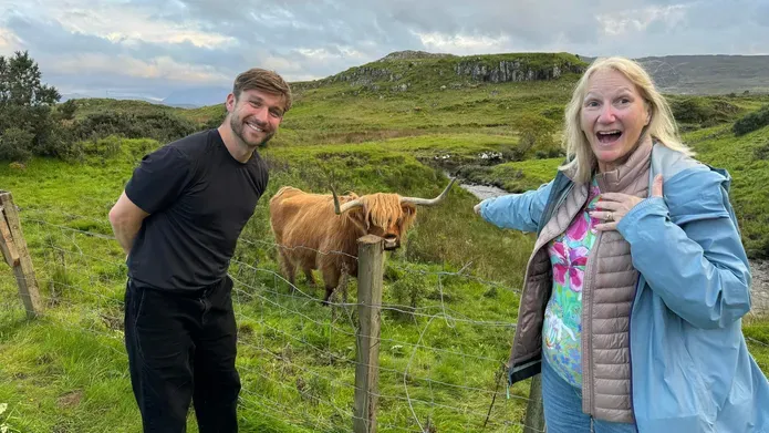 man and woman standing in front of green field with highland cow between them
