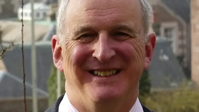 Professor Nigel Seaton, smiling while wearing a suit and tie. The Tay Bridge is in the backround.