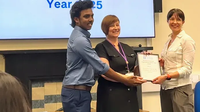 Student poses with two ladies, all smiling and holding event lanyards, suggesting participation in a student event