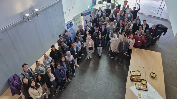 : Large group of students and academics standing and smiling at the camera, looking up wards as the picture is taken from height