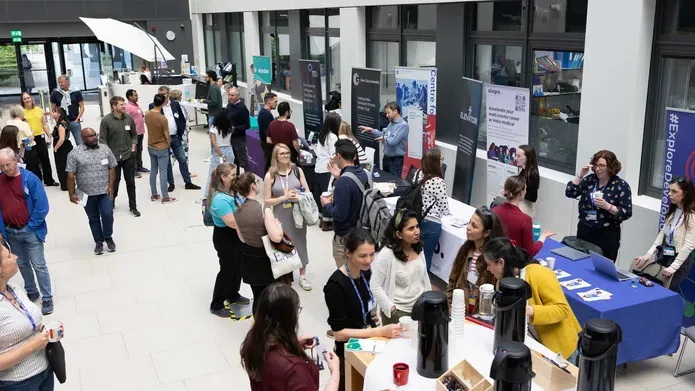 A room with lots of people standing around, there are tables set up with merchandise and banners.