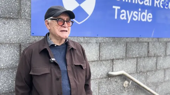 Brian Cox stands in front of School of Medicine sign at Ninewells