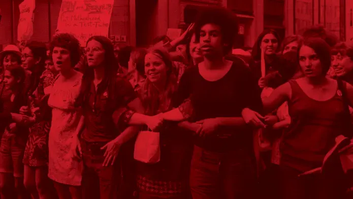 Photograph with red tint. A crowd of women stand linked arm-in-arm at a protest
