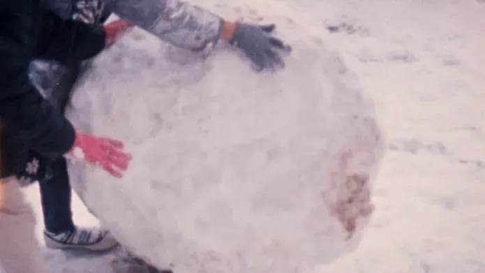 Film still. Gloves rolling a giant snowball