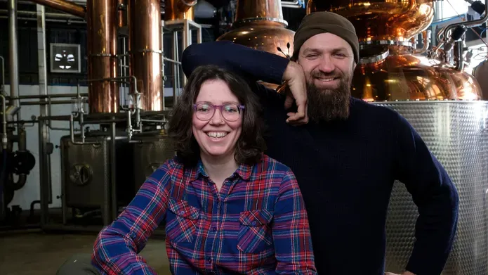 A man and woman sat in front of brewing equipment