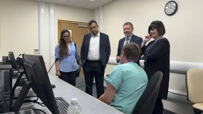 Dr Vikas Swarankar standing in room beside three people listening to a seated person in scrubs.