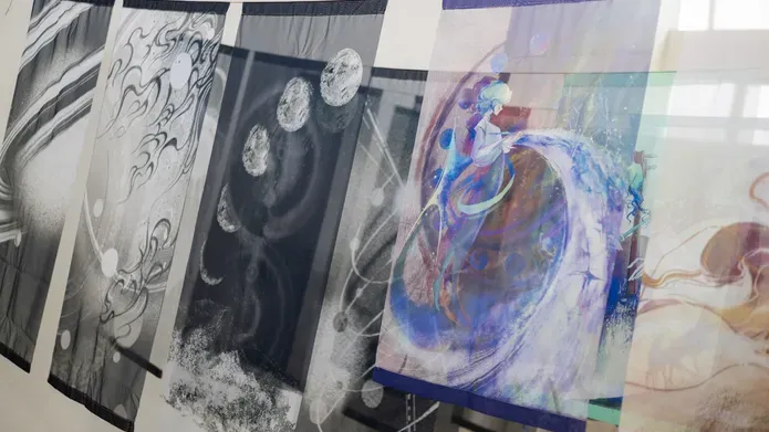 close up image of transparent flags hanging in rows. Most are black and white with planets on them and one on the right hand side is brightly coloured in blues and purples with the image of a figure on it