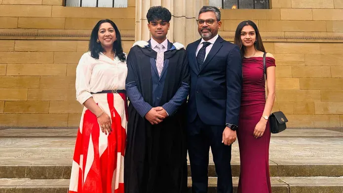 A students on graduation day posing with his family, smiling and all standing on steps outside a building, all dressed in smart wear.