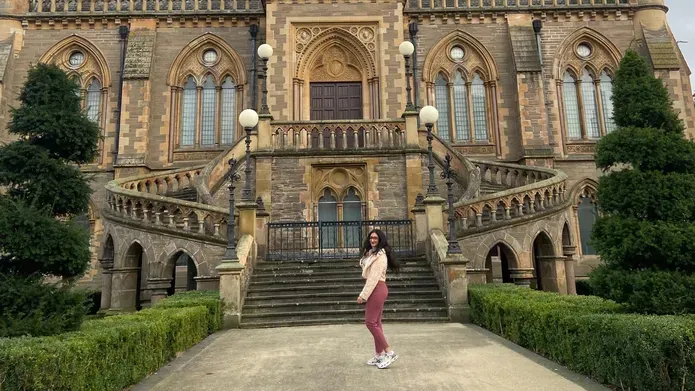 A student, with a cream jacket, dark pink legging and trainers standing outside a museum and smiling at the camera