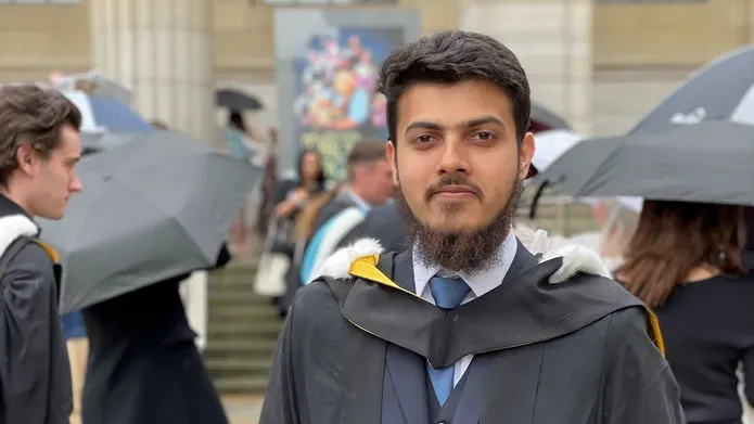 A graduate standing outside of Caird Hall in graduation regalia