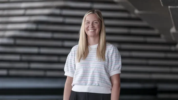 woman wearing woollen tshirt, with long blond hair, looking and smiling at camera