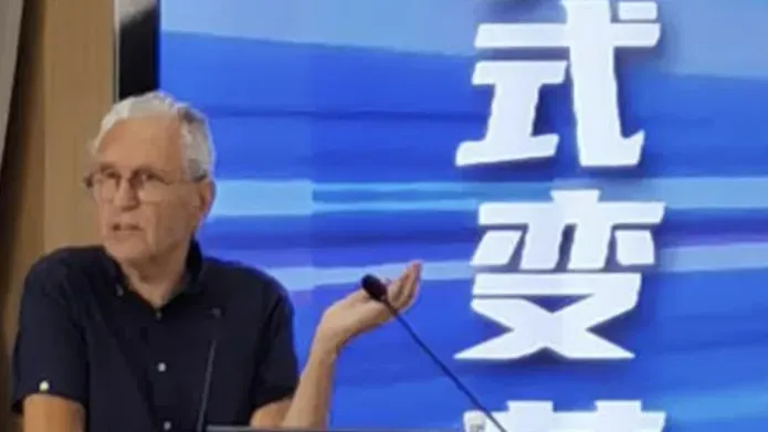 A man stood at a lectern in front of a screen featuring chinese writing