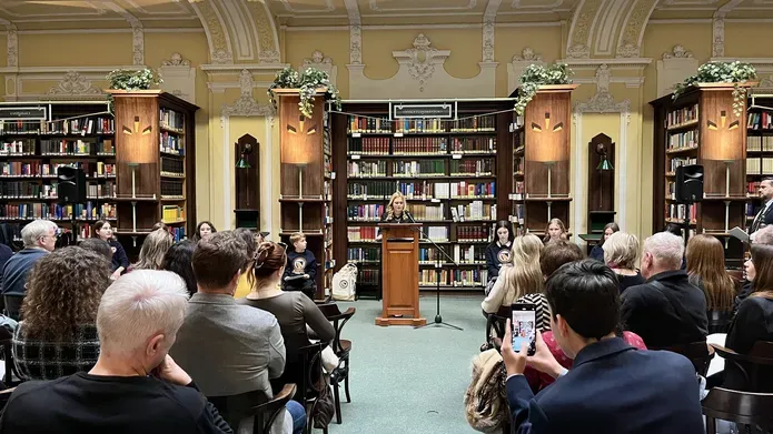 Sara Turnbull standing at a wooden podium in front of a room full of people.