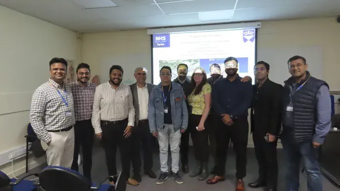 A group of people stand in front of a smart board screen in a classroom.