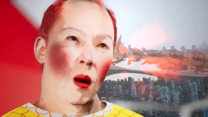 Digital video still. A close-up CGI rendering of an asian man with white make-up on his face, rouge on his cheeks and dyed short red hair. Over his should we can see two types of landscape. Rows of skyscrappers and above this red amorphous shapes floating in a digital pink hued sky.