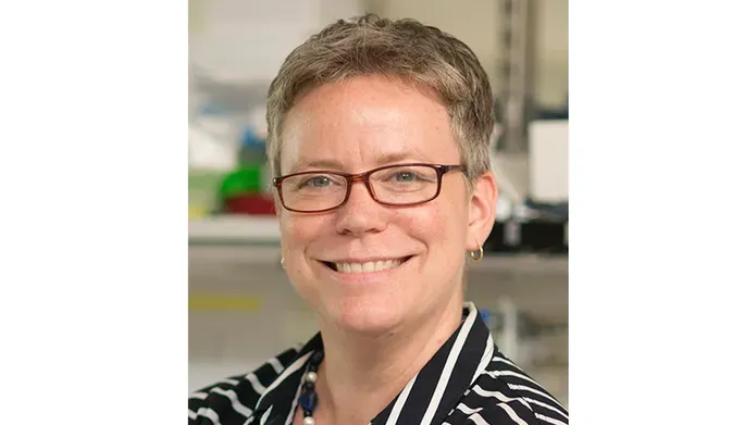 A head and shoulder shot of a woman with short hair and wearing glasses who is smiling