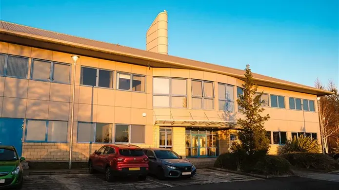 A brown building with lots of windows and two cars parked outside on a blue sky day.