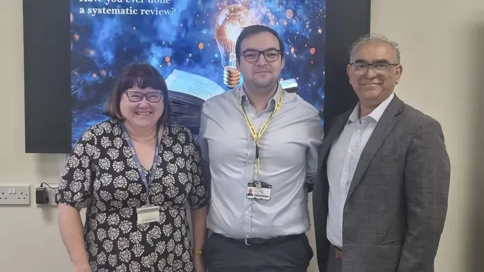 Three people stand in front of a screen with the words: "Have you ever had a systematic review?"