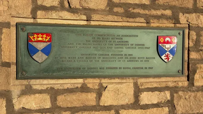 plaque to commemorate association of University of Dundee with St Andrews, on a brick wall. Crests from both universities are visible.