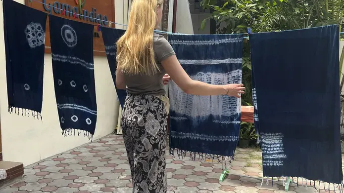 A blonde woman stands at a washing line with pieces of white and indigo patterned fabric.
