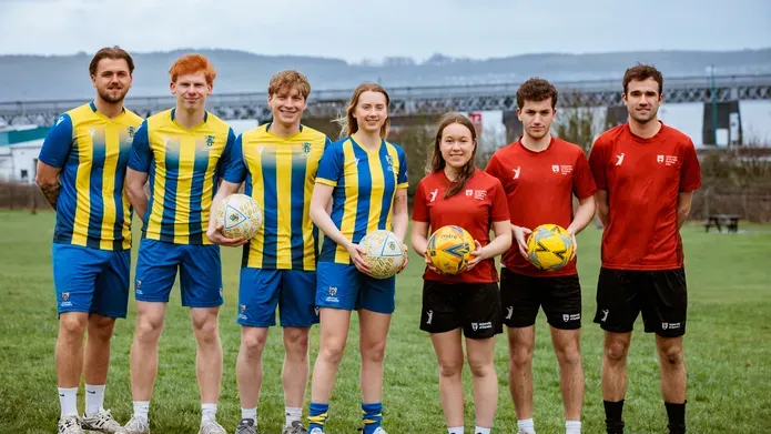 two football teams standing side by side, one with a red strip and the other with a blue and yellow striped top