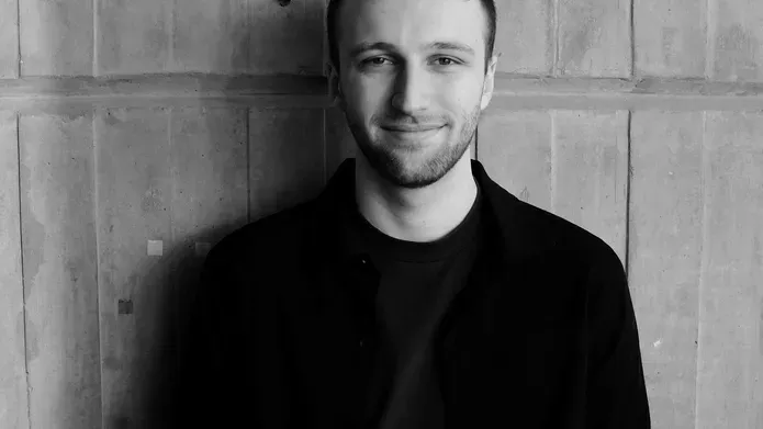 A black and white image of Drew Rumgay against a concrete wall