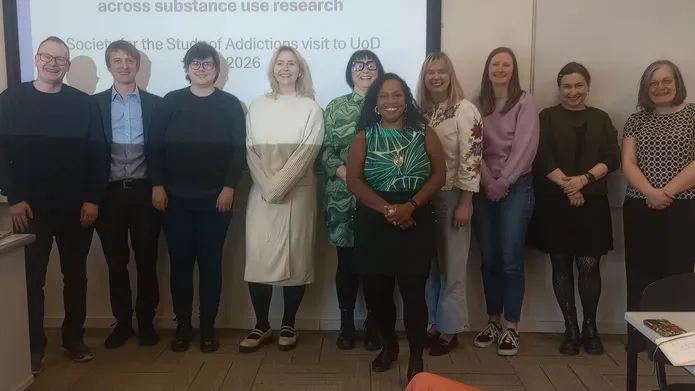 A group of people stand in front of a wide screen with the text Substance Use Research Group (SURG) in Health Sciences 