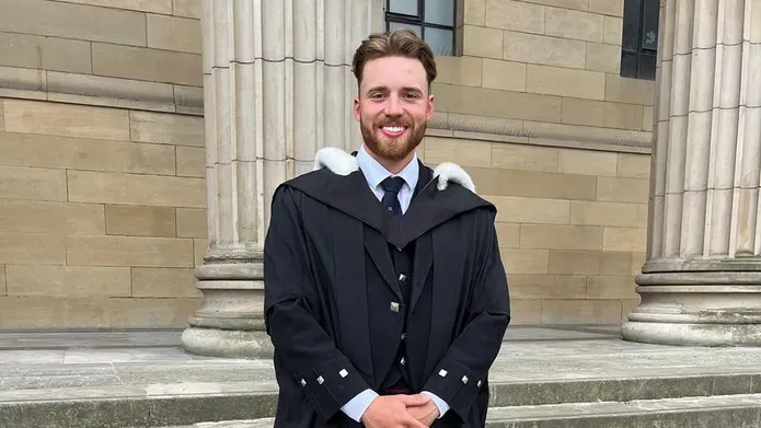 Adam Hall in graduation robes on the steps of the Caird Hall