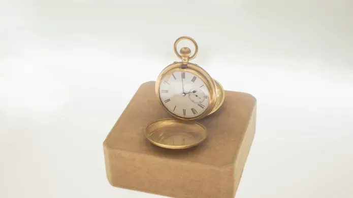 A gold pocket watch on a plinth against a white backdrop