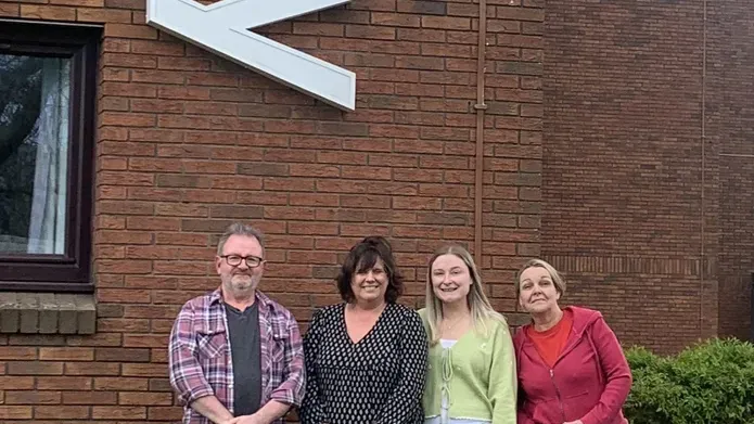 Members of staff from Kirkcaldy campus stand against a brick wall, smiling.