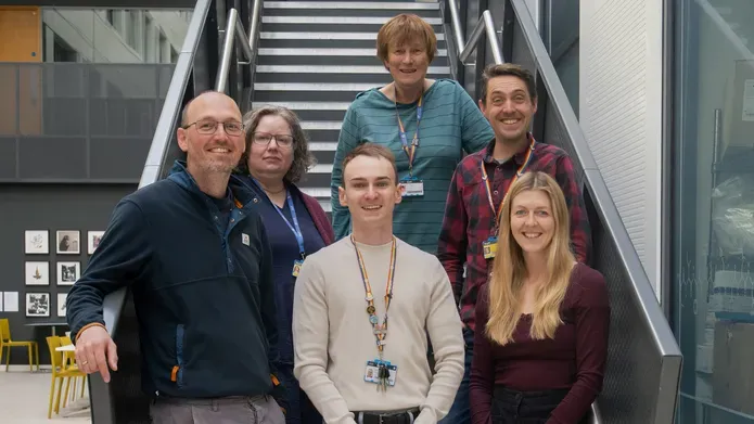 Six people stood together smiling while stood on a staircase