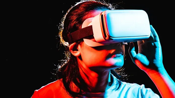 Person wearing a virtual reality headset illuminated by blue and red neon lighting against a dark background