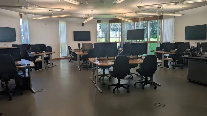 An IT lab in the Queen Mother building with office chairs, desks and computers