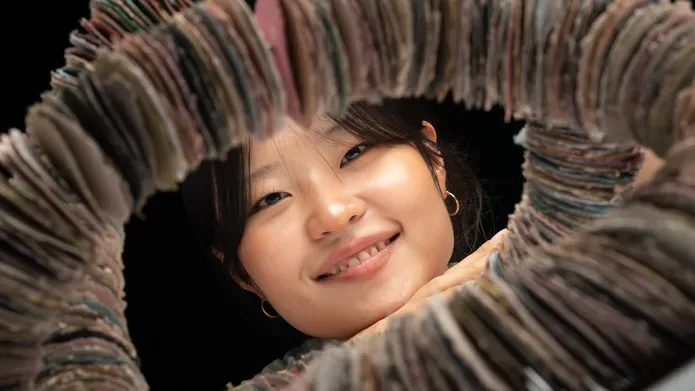 A headshot of Nayoung, smiling, whilst looking through a circle of her ceramic discs.