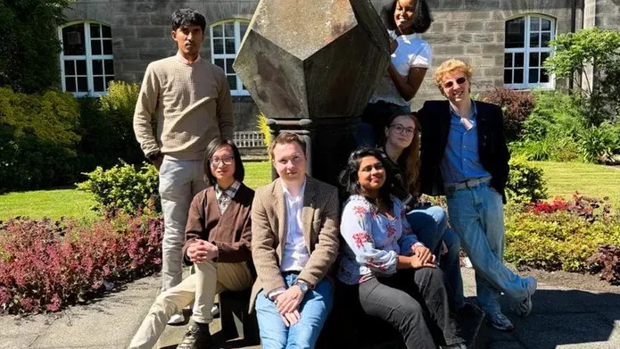 Members of the DUSA exec posing around a sundial in the Geddes Quad on a sunny day