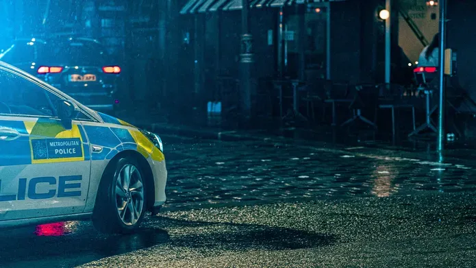 A police car parked at night on a cobbled street
