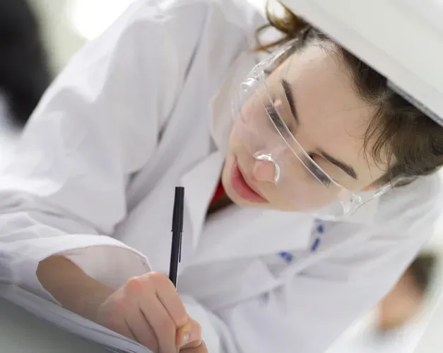 Student in white coat in lab at a machine