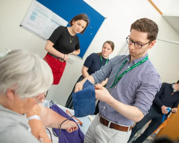 Medical student taking the blood pressure of a patient while others observe