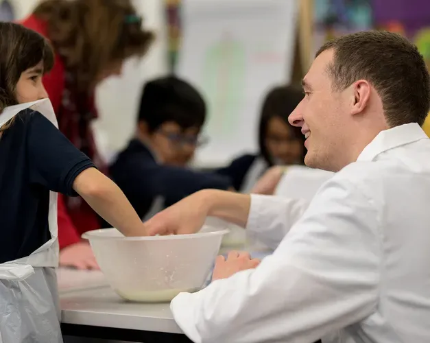 A teacher helping a girl mixing something in a bowl