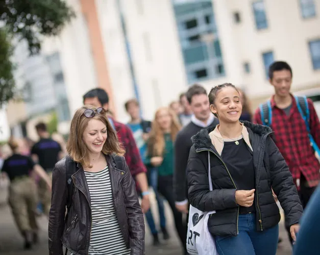 students walking on campus, two people at the forefront are smiling