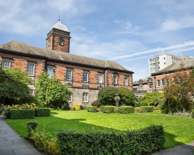 a red stone building with grass, seating and hedges out the front