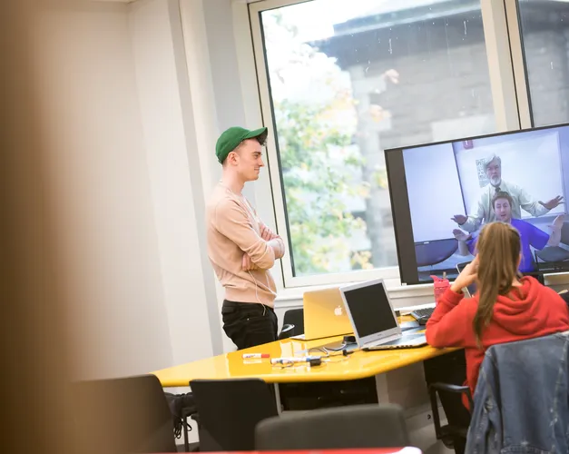 Students work at a table with a large TV screen at the end attached to a computer