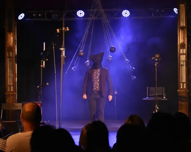 Kevin Quantum standing under blue smoke stage lights with a sack on his head